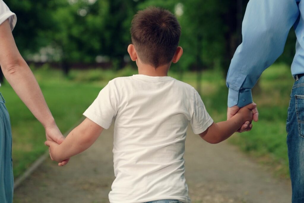 enfant marchant main dans la main avec sa mère et son père adoptifs